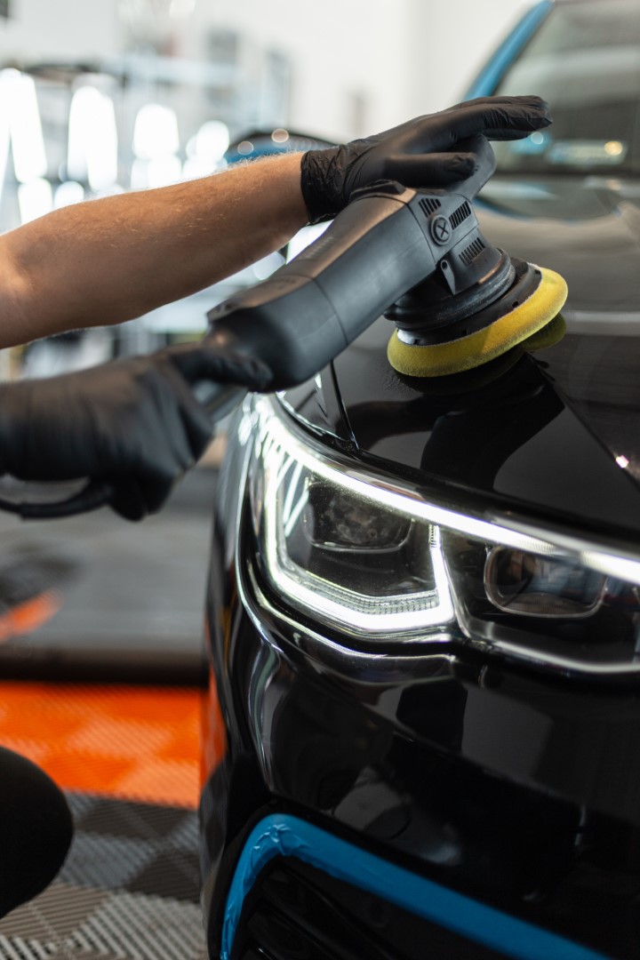 Professional man with polishing machine polishes car varnish with optics in detailing studio