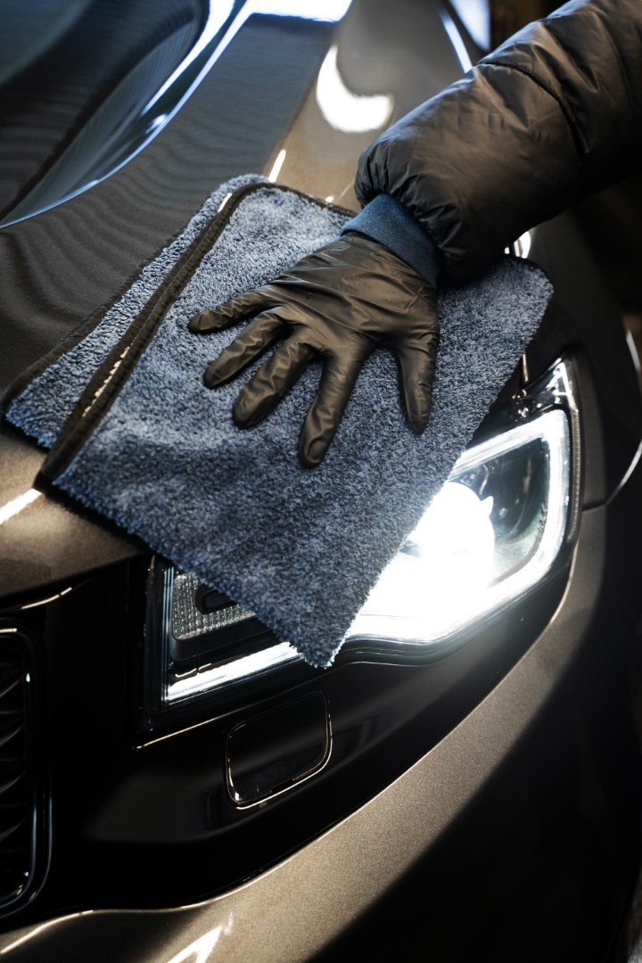 Wiping car body using a microfiber cloth. Polishing car headlight during detailing services. The process of car valeting