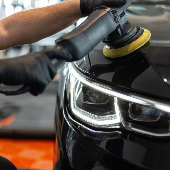 Professional man with polishing machine polishes car varnish with optics in detailing studio
