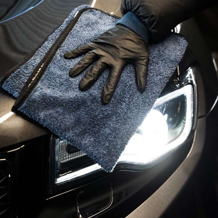 Wiping car body using a microfiber cloth. Polishing car headlight during detailing services. The process of car valeting